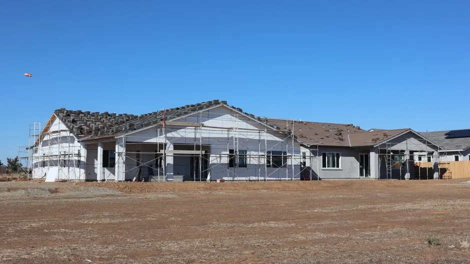 A house under construction with scaffolding on a sunny day, clear blue sky.